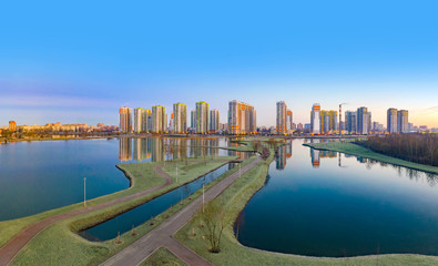 Fototapeta premium Residential complex on the shore of the lake. Modern urban architecture. Apartments in new buildings near the recreation area. Urban landscape. Ponds and houses under a blue sky.