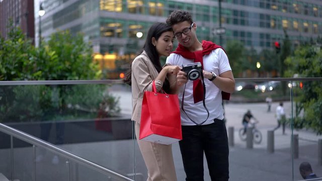 Happy male and female checking images on old fashioned equipment during recalls of positive moments, smiling couple in love watching on pictures after shopping time in downtown
