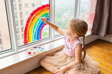 Kid painting rainbow during Covid-19 quarantine at home. Girl near window. Stay at home Social...