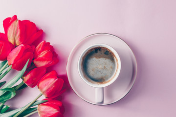 Pink cup of coffee and real tulip flowers on a pink background. Flat lay. Female workplace with cozy breakfast
