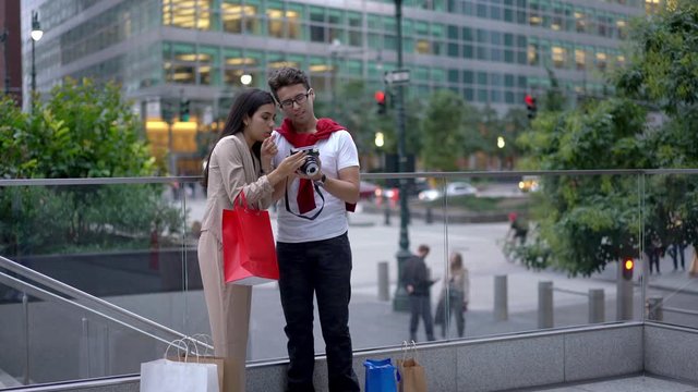 Latino American hipster guys taking pictures of themself while resting on urban setting after shopping time during weekend, stylish couple in love using old fashioned camera for clicking selfie
