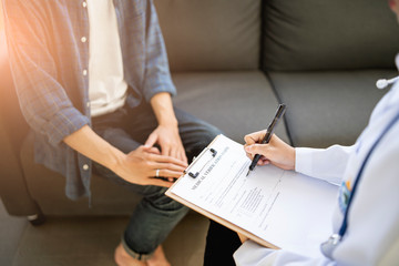 close up of asian female doctor witting on a documentation on a clipboard on diagnosing patient health or filling in a medical verification form of the patient, sitting in hospital office medical room
