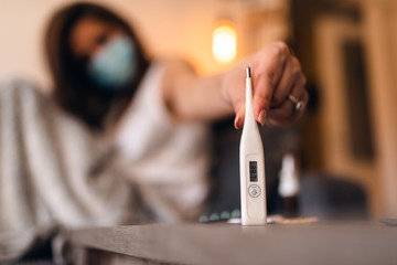 Close up of a thermometer on the table while in the background is a girl with a mask