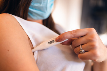  A beautiful caucasian sick woman with a mask measures her temperature