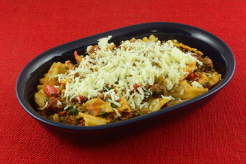 Lasagna casserole with hamburger meat, spinach, tomatoes, onion, and green bell peppers smothered with shredded cheese in blue serving bowl on red