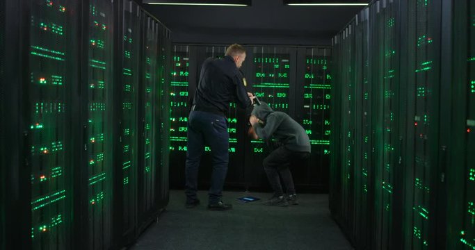 Caucasian policeman pointing gun at criminal who committing cyber crime in server room and breaking into system. FBI officer arresting hacker while man hacking database. Catching cyberdata thief.