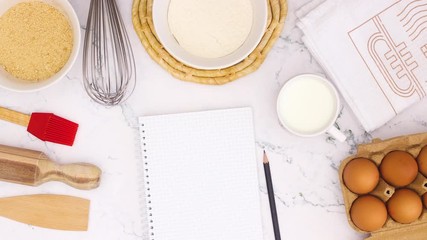 Cooking supplies appear on marble table and notebook for recipe - Stop motion 