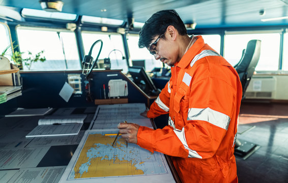 Filipino deck Officer on bridge of vessel or ship wearing coverall during navigaton watch at sea . He is plotting position on chart