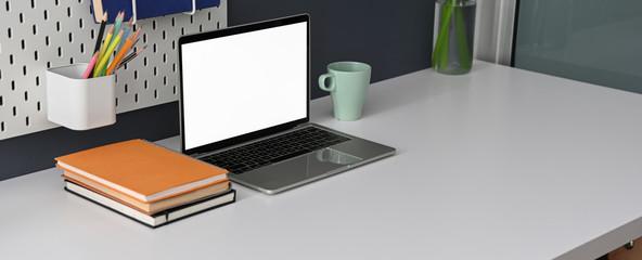 Cropped shot of comfortable office desk with blank screen laptop, notebooks, stationery and copy space
