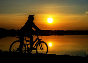 Silhouette of a girl on a sports bike by the lake against the background of the sunset