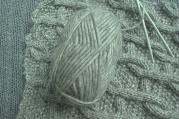 Knitting needles with ball of wool, dark blanket and grey wool background.