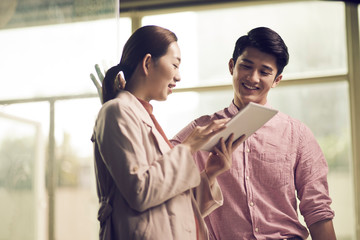 two young asian entrepreneurs discussing business in office using digital tablet