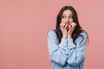 Image of scared brunette woman frowning and biting her nails