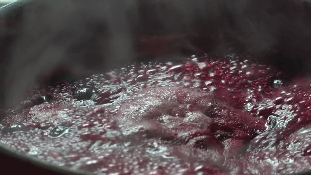Cooking delicious red fruit jam, mixing and kneading. Close up. Jabuticaba or jaboticaba jam. Cook jaboticaba, which boils and foam in a ceramic lined pan.