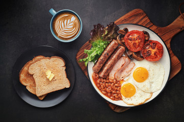 Full English Breakfast with Latte Art on dark table sausage eggs bean bacon tomatos mushroom