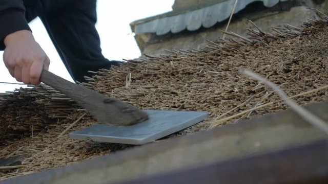A Man Holding A Leggett And Layering The Thatched Roof. _closeup shot