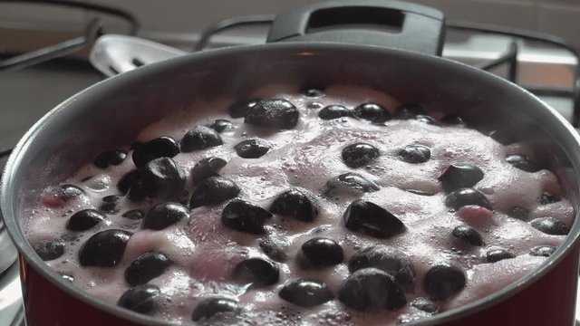 Cooking delicious red fruit jam, mixing and kneading. Close up. Jabuticaba or jaboticaba jam. Cook jaboticaba, which boils and foam in a ceramic lined pan.