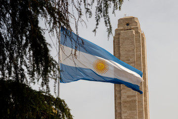 Fototapeta premium Flaga Argentyny widziana między gałęziami drzew przed wieżą pomnika flagi narodowej w Rosario w Argentynie