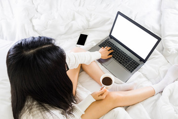 Topview of young  asian woman wear white knitwear dress on bed,working with blank screen laptop from home,drinking coffee, Selective focus