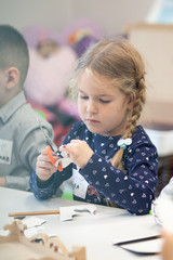 A little girl cuts out paper with scissors, a child is engaged in creativity, a preschooler makes crafts, Children's creativity at home and in kindergarten.