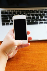 Man's hand working remotely with smartphone have laptop on wooden table. Working remotely concept.