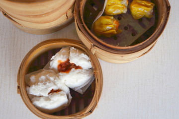 Top view of Chinese steamed red pork bun break can see pork inside and Cantonese Shumai (Siu Mai) wrap by yellow wonton wrapper (Kanom Jeeb in Thai) in bamboo basket in dim sum set