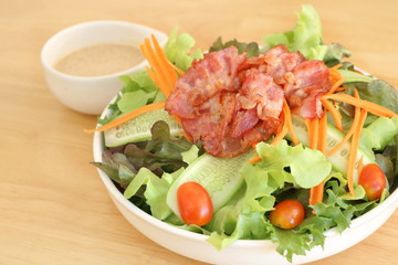 Close up fresh vegetable salad (lettuce, carrot, cucumber, tomato)  with fried bacon and roasted sesame Japanese dressing in white bowl on wooden table background