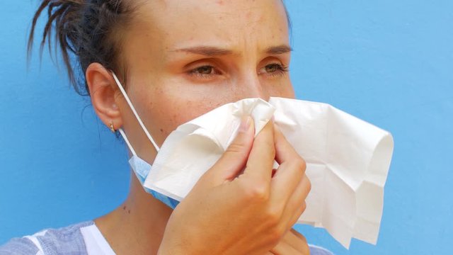 A young woman in a mask blows her nose with a paper napkin
