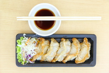 Fried Gyoza, Japanese dish consisting of wonton wrappers stuffed with pork and cabbage, eat with soy sauce, on wood table