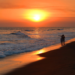 Obraz premium Sunset panorama along the volcanic sand beach of Monterrico with unrecognizable people by the Pacific Ocean, Guatemala.