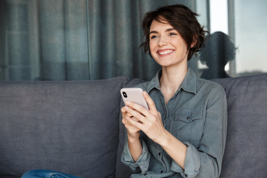 Image of beautiful young joyful woman using mobile phone and smiling