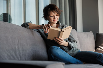 Image of brunette cute focused woman reading book and smiling