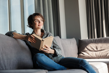 Obraz premium Image of brunette cute pleased woman reading book and smiling
