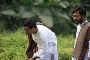 Young Indian Bengali detective and his colleague with traditional wear finding some clue in a grass field in a winter morning. Indian lifestyle.