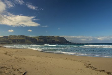 evocative image of sandy beach with rough sea headland in the background and clouds