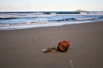Fototapeta na wymiar evocative closeup image of abandoned buoy on sandy beach with rough seas and small island in the background