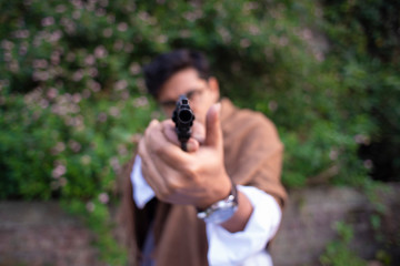 Blurred portrait of an young Indian Bengali detective with traditional wear pointing a gun in a winter morning in a crime scene.