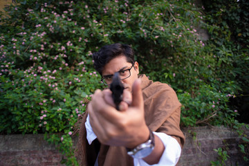 Blurred portrait of an young Indian Bengali detective with traditional wear pointing a gun in a winter morning in a crime scene.