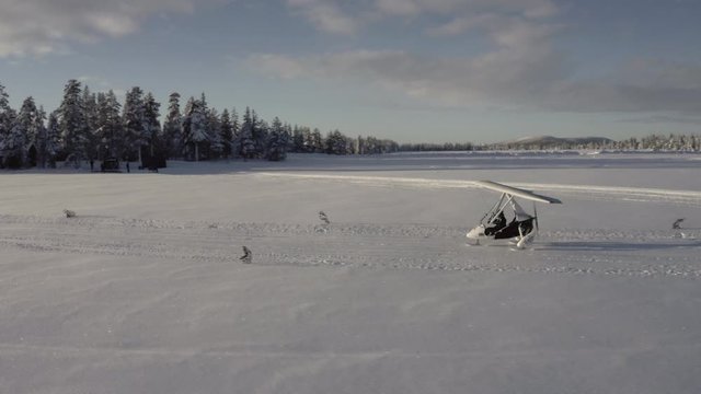 A drone shot flying past a microlight or flexwing taking off from a snow runway (frozen lake) in Sweden.  Microlight is on skis in the snow rather than wheels.