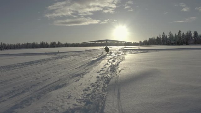 A drone shot of a microlight or flexwing taking off from a snow runway (frozen lake) in Sweden.  Microlight is on skis in the snow rather than wheels.