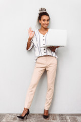 Happy young african business woman with dreads isolated over white wall background using laptop computer showing okay gesture.