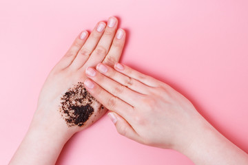 Women's hands apply coffee scrub, pink background, the view from above