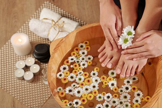 Woman Putting Feet In Wooden Basin With Water And Small Flowers For Making Pedicure