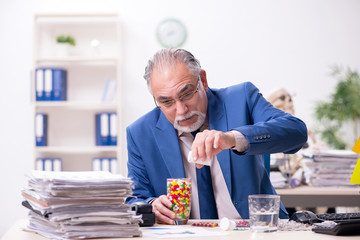 Old male sick employee working overtime in the office