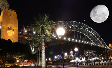 Sydney harbour illuminated by the moon and circular quay with vibrant colourful lights at midnight in NSW Australia