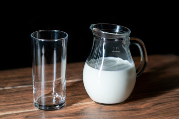Una taza de cristal vacía y una jarra de leche de vaca en una mesa de madera