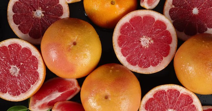 Whole and pieces of fresh grapefruit slowly rotate.