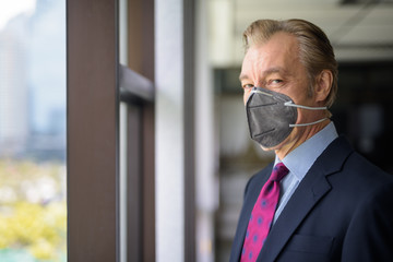 Mature businessman with mask for protection from corona virus outbreak by the window at work