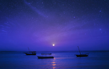 Märchenhafte Nachtlandschaft Afrika, Tansania, Sansibar. Silhouette von Fischerbooten auf dem Hintergrund des Sternenhimmels im Ozean