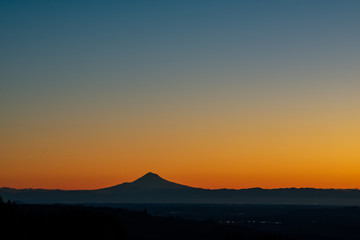 A sunrise scene in Oregon, with the iconic peak of Mt. Hood on the horizon in silhouette, vivid color behind.